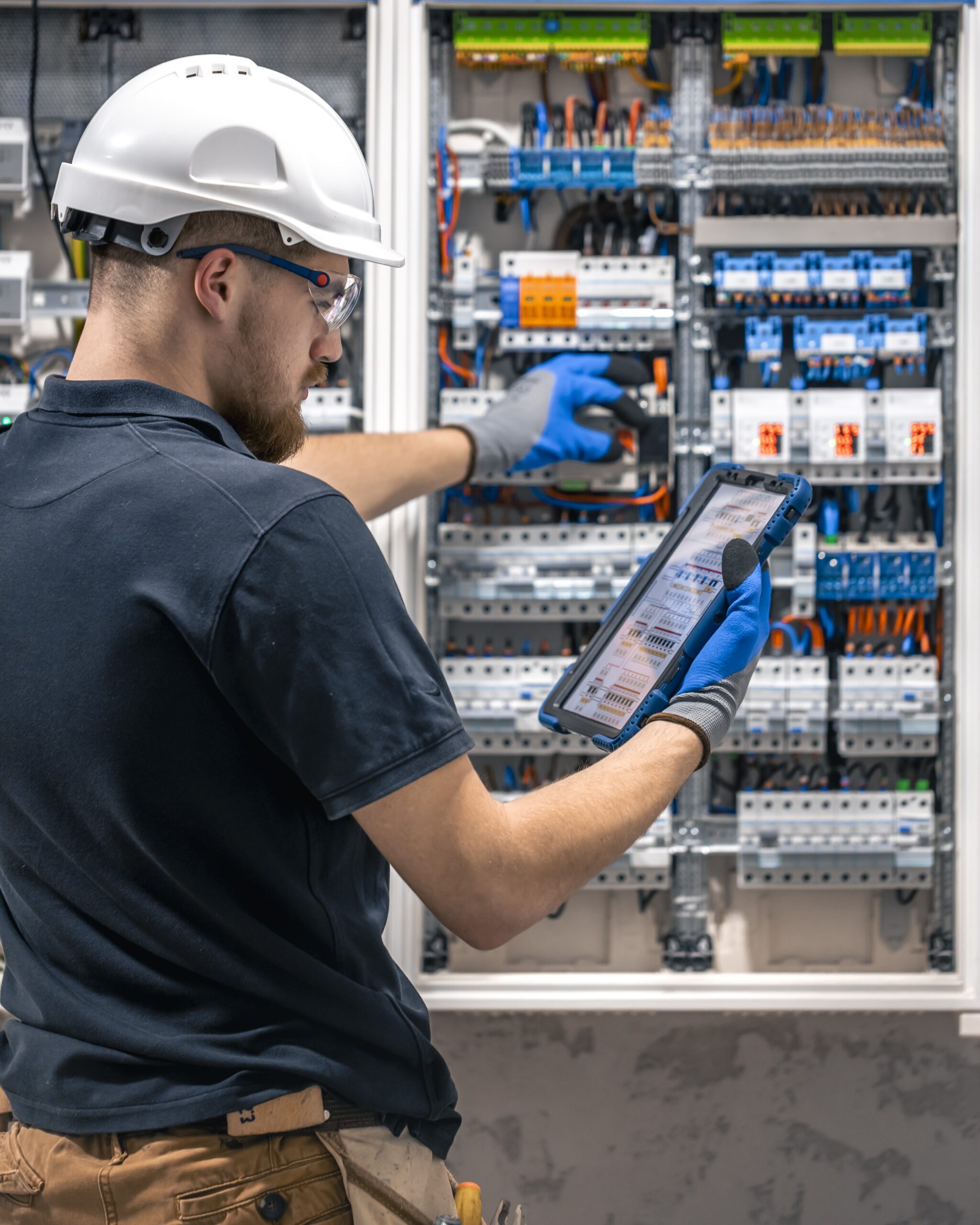 Electrical technician working in a switchboard with fuses, uses a tablet.